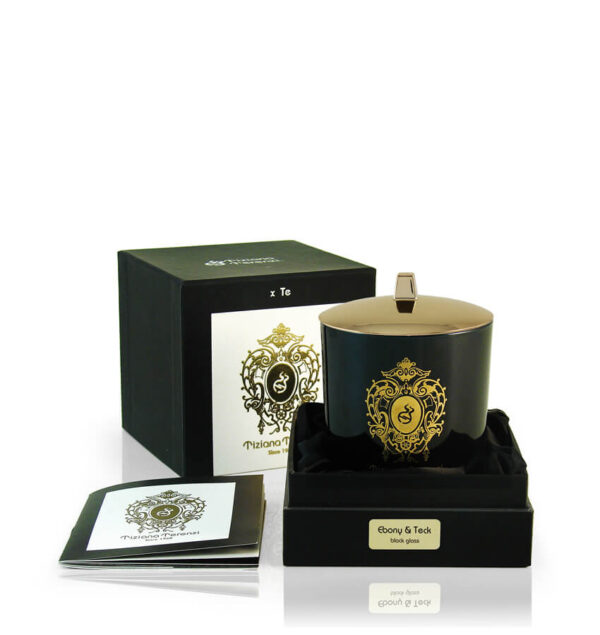 Candela Tiziana Terenzi Ebony & Teck in vaso di vetro nero con coperchio lucido e decorazione dorata. La candela è presentata in una confezione nera elegante, con il logo distintivo Tiziana Terenzi e un opuscolo informativo a lato, risaltando l’artigianato italiano dal 1968.